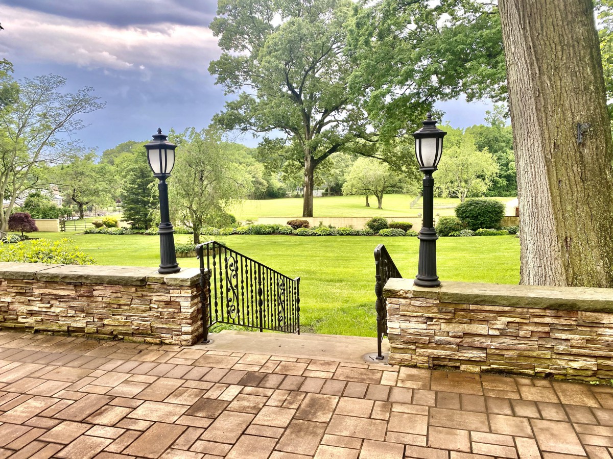 A scenic view from a patio overlooking a lush garden with stone walls and traditional lamps.