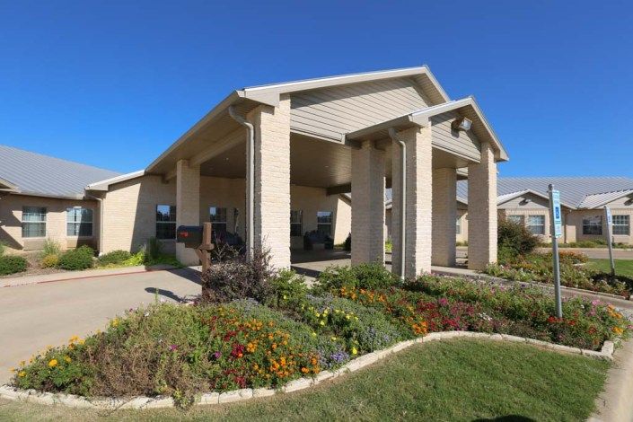 A modern building exterior with a landscaped garden and prominent columns.