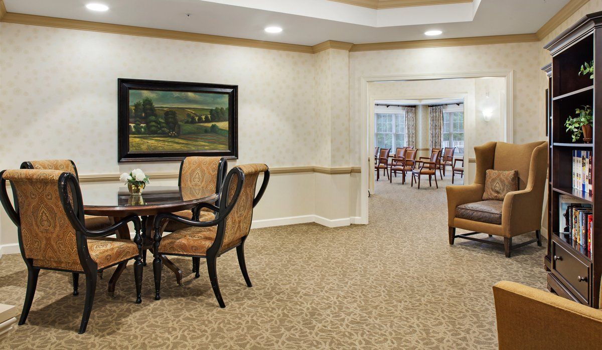 A well-furnished dining area with a round table, upholstered chairs, and artwork on the wall.
