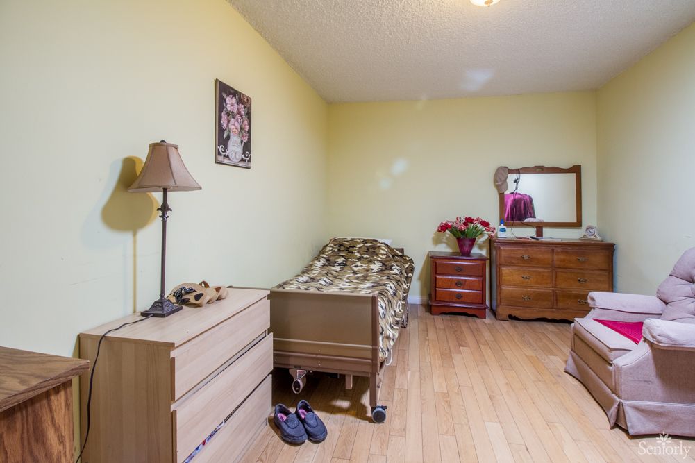 A small bedroom with a single bed, dresser, and mirror on a hardwood floor.