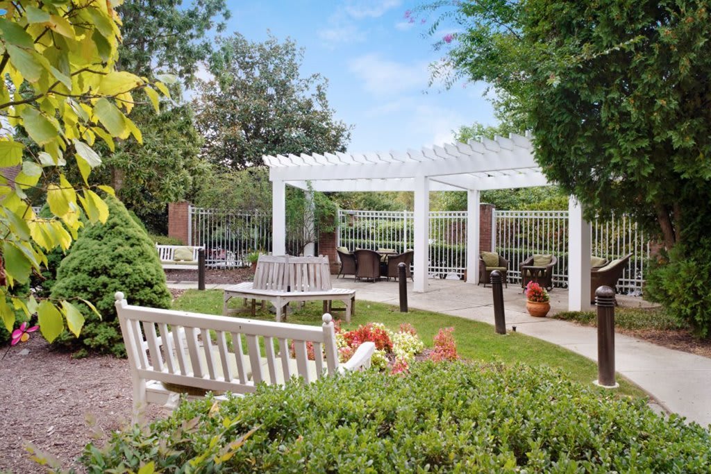 A serene garden with a white pergola, outdoor seating, and lush greenery.