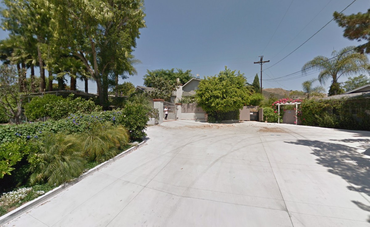 A suburban driveway leading up to a house surrounded by trees.