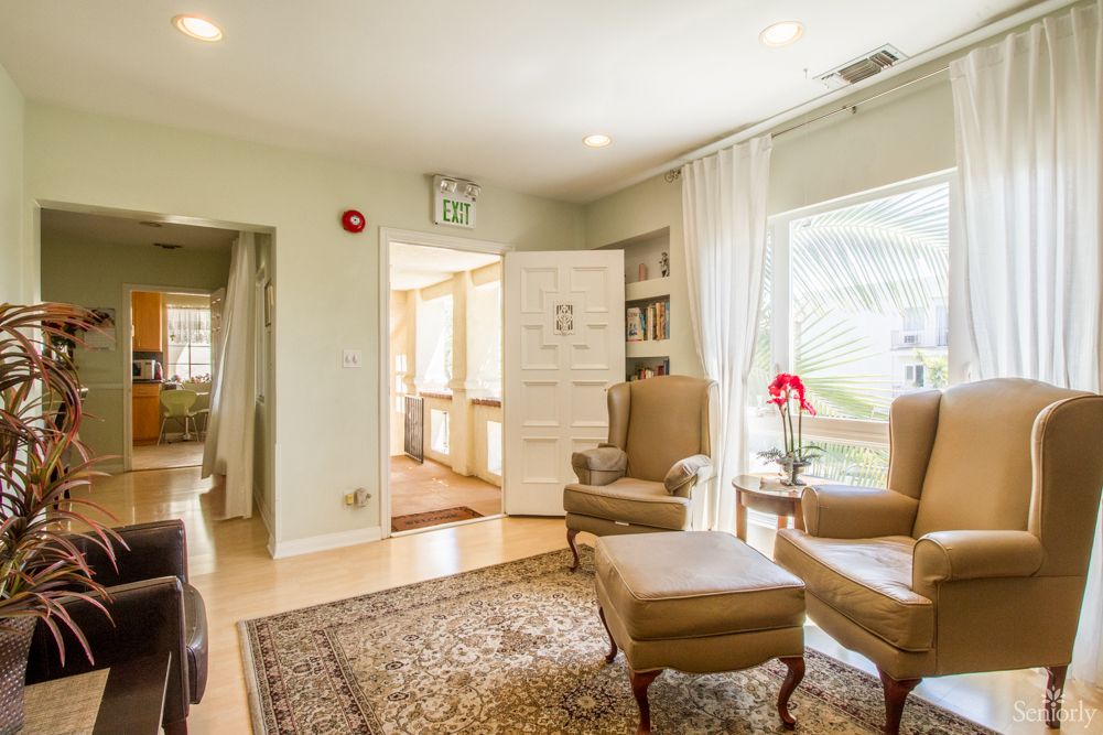 A bright and cozy living room with comfortable armchairs, a patterned rug, and large windows letting in natural light.