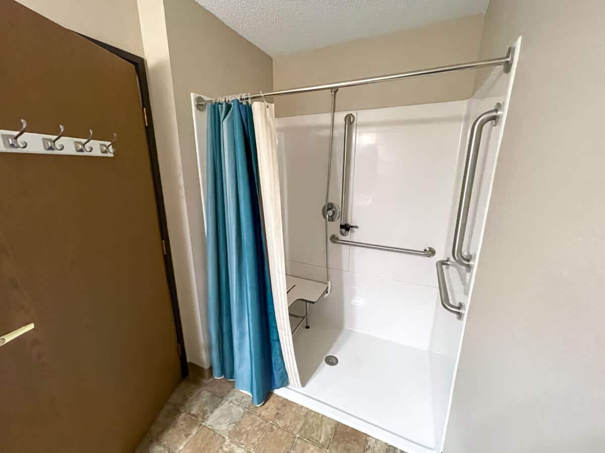 An accessible shower with grab bars and a blue curtain.