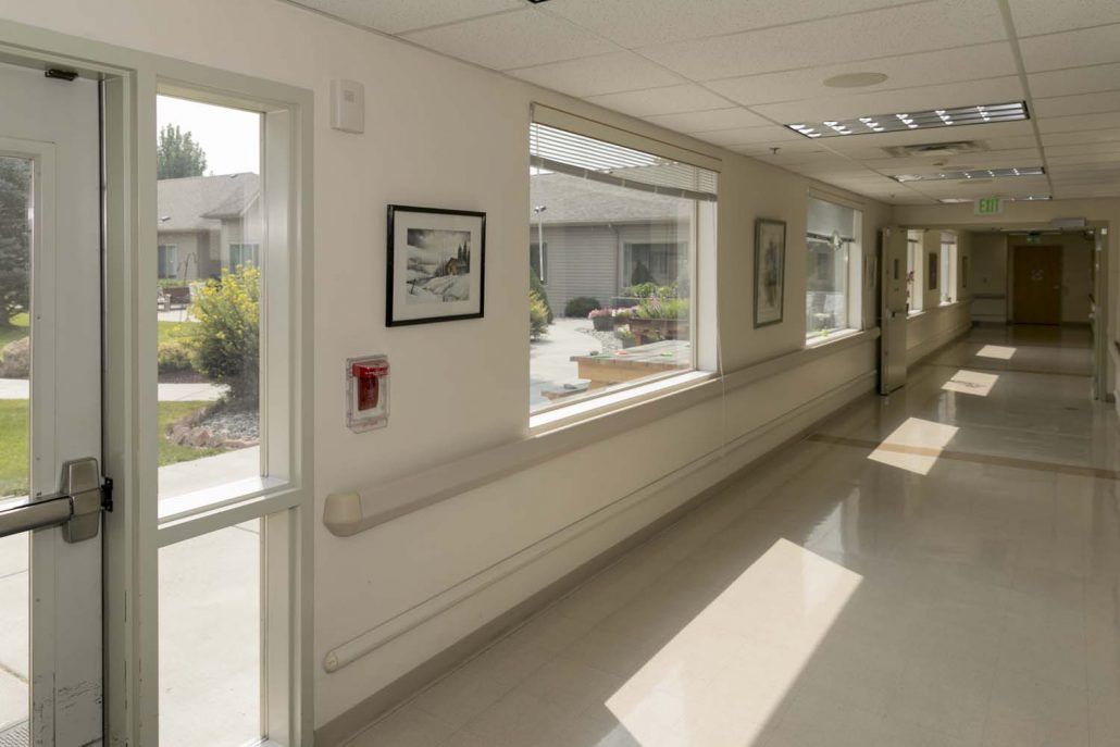 A sunlit hospital hallway with large windows and artwork on the walls.