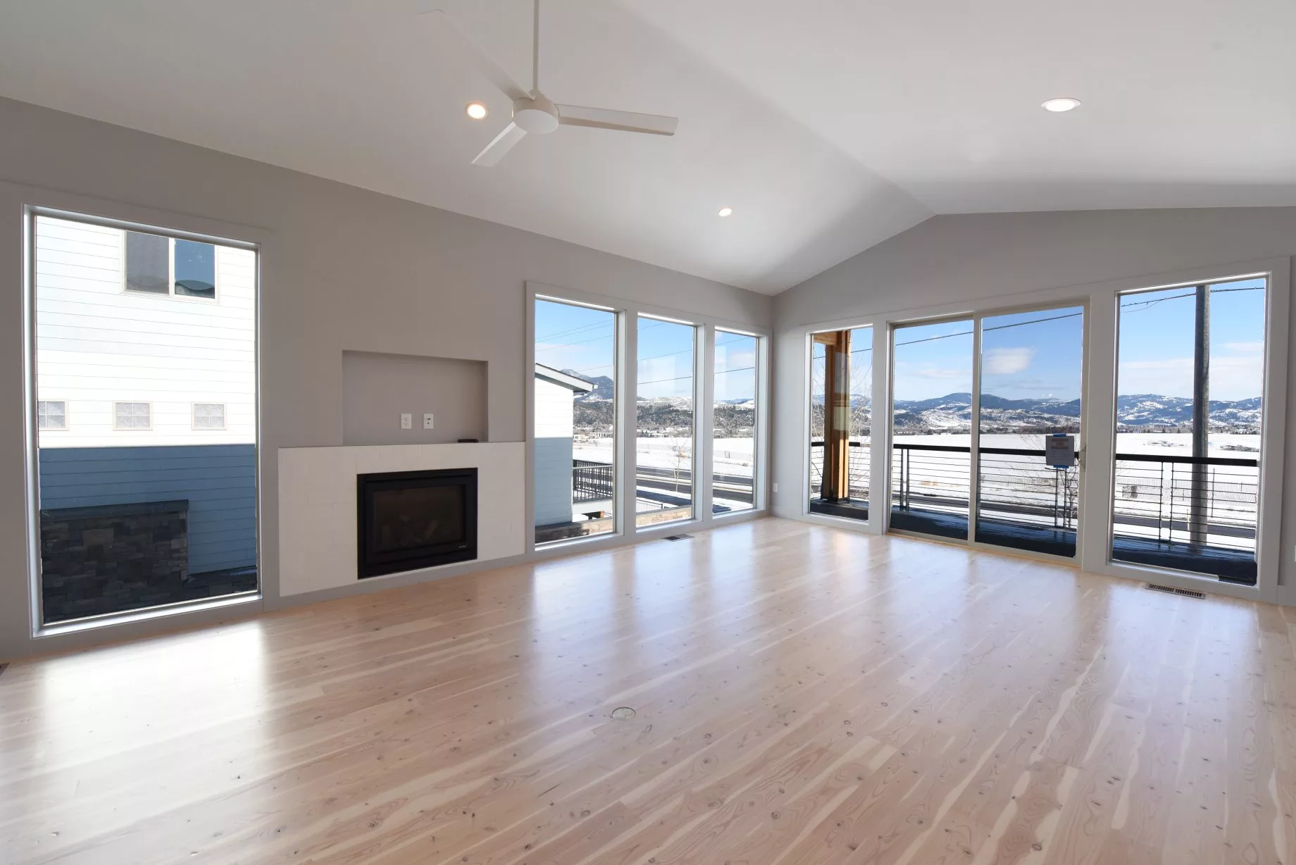 A modern living room with hardwood floors, large windows, and a fireplace.