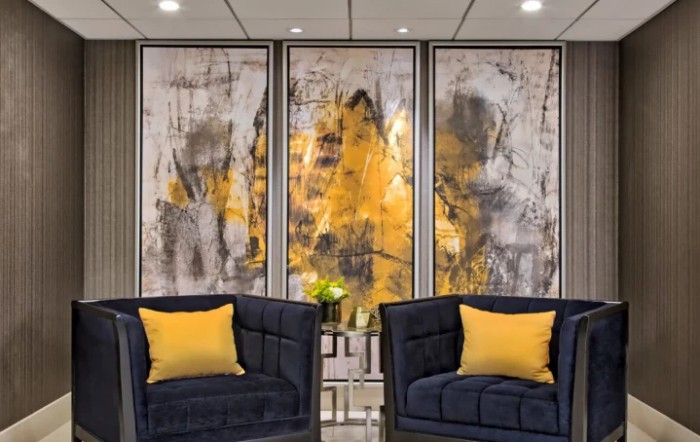 A modern interior with two luxury chairs in front of abstract triptych artwork featuring yellow and gray hues.