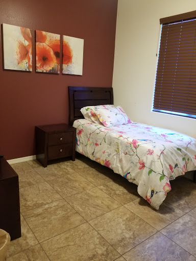 A cozy bedroom featuring a single bed with floral bedding, a nightstand, and decorative artwork on the wall.