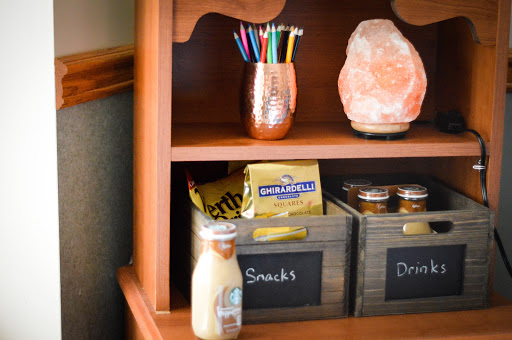 A cozy shelf featuring a collection of snacks, colorful pens, and a decorative salt lamp.