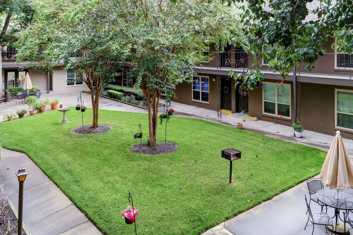 A serene apartment courtyard with well-maintained grass and trees.