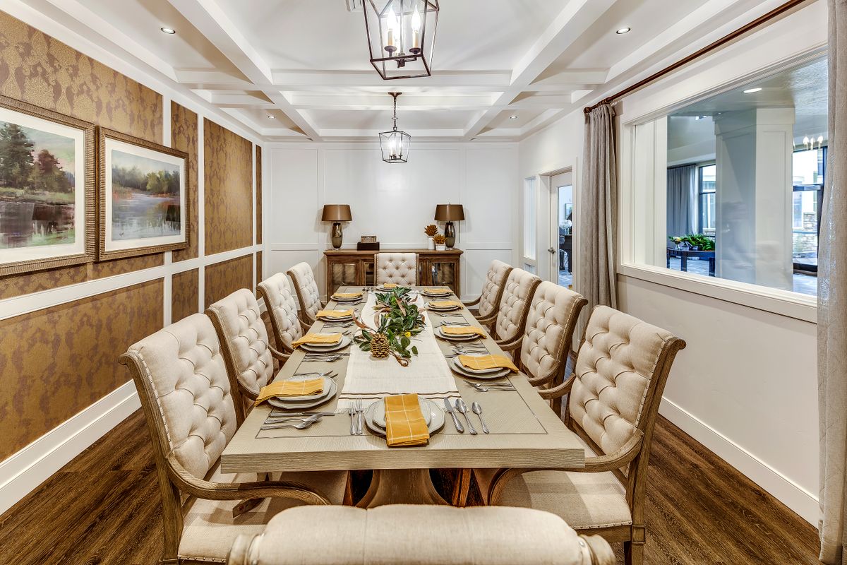 An elegantly designed dining room with a long table set for dinner, featuring upholstered chairs and warm neutral tones.
