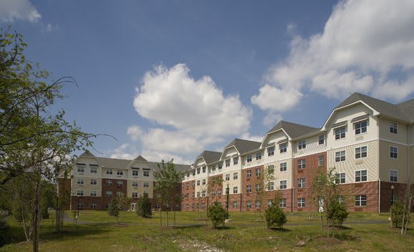 A large residential apartment building with a grassy lawn under a partly cloudy sky.