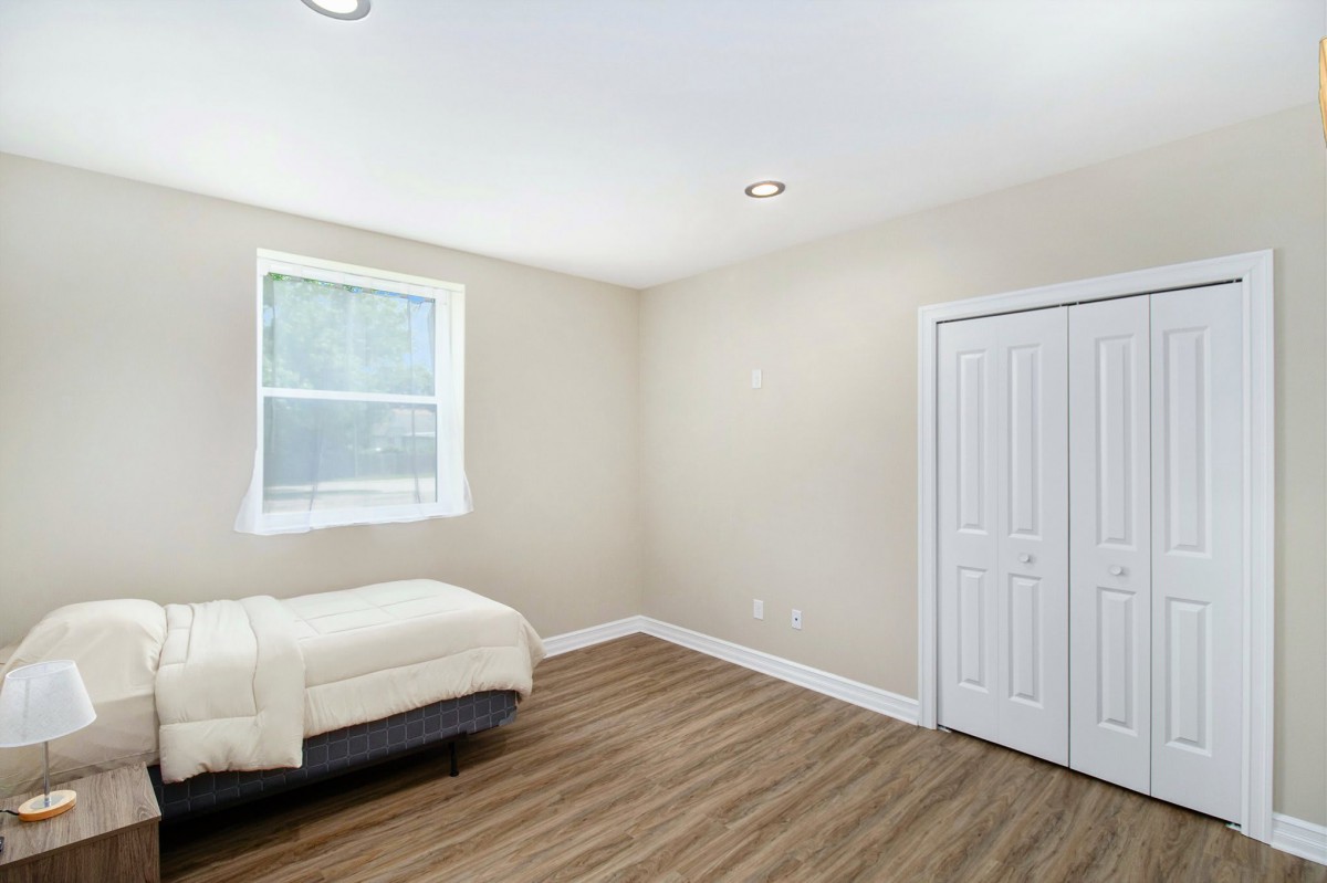 A minimalist bedroom with a single bed, wooden flooring, and beige walls.