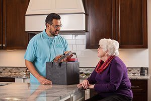 A delivery person brings groceries to an elderly woman in her kitchen.