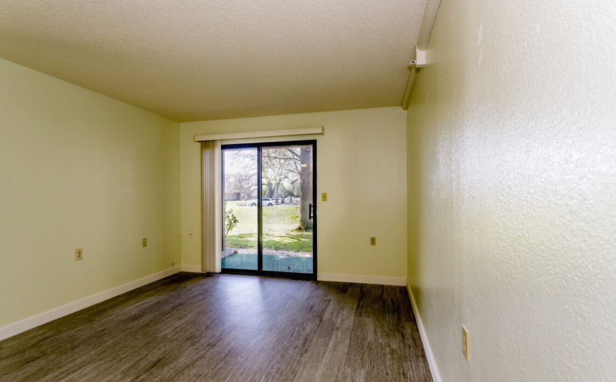 An empty living room with hardwood flooring and a sliding glass door leading to an outdoor area.