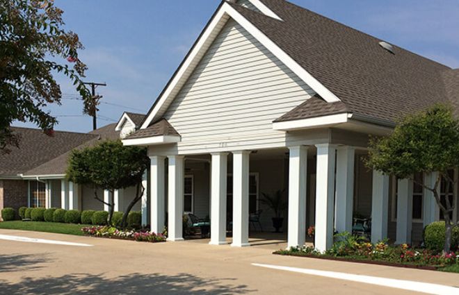 A building with a pitched roof and white columns at the entrance, surrounded by landscaping.