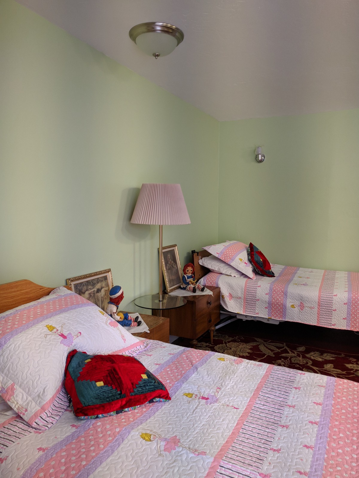 A cozy bedroom with twin beds featuring pink patterned bedding, a lamp on the nightstand, and a decorative rug.