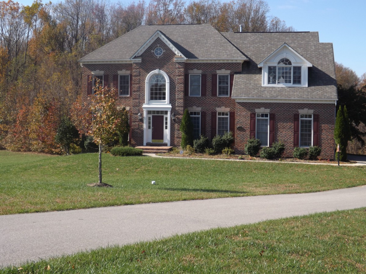 A large suburban brick house with a well-maintained lawn and paved driveway.