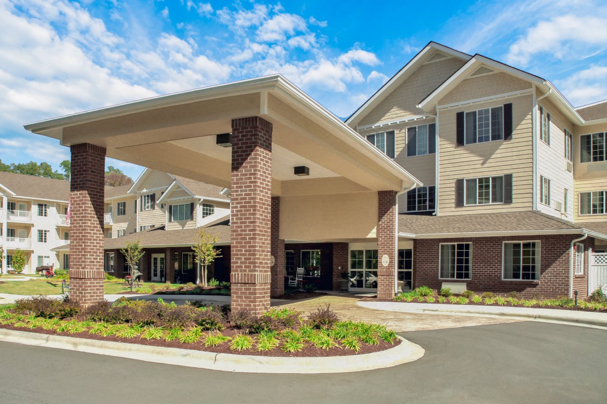 A well-maintained retirement home with a covered entrance, surrounded by landscaped greenery on a sunny day.