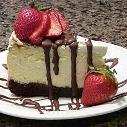 A delicious slice of cheesecake topped with strawberries and chocolate drizzle.