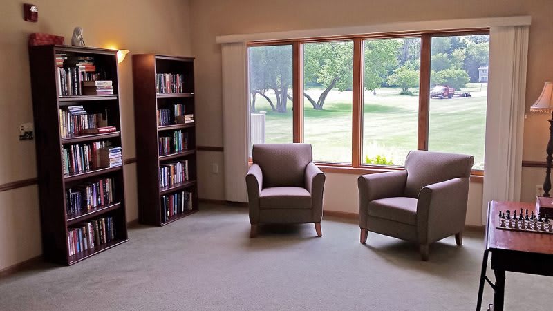 A cozy living room with two armchairs and a bookshelf by a large window.