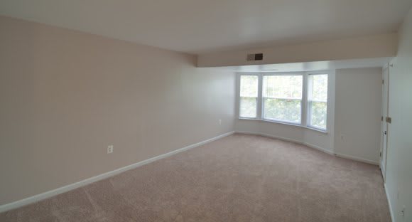 An empty room with carpet flooring and a bright bay window.