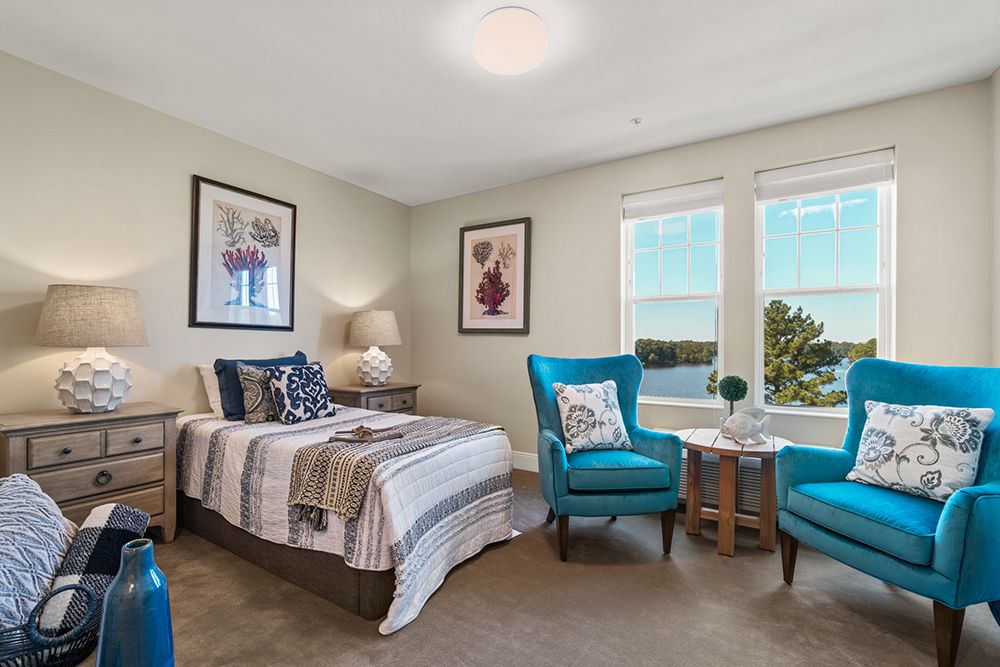 A cozy bedroom featuring a bed with striped linens, two turquoise chairs, and artwork on the walls.