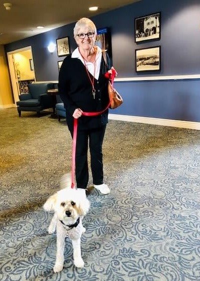 A person indoors holding a small dog on a red leash.