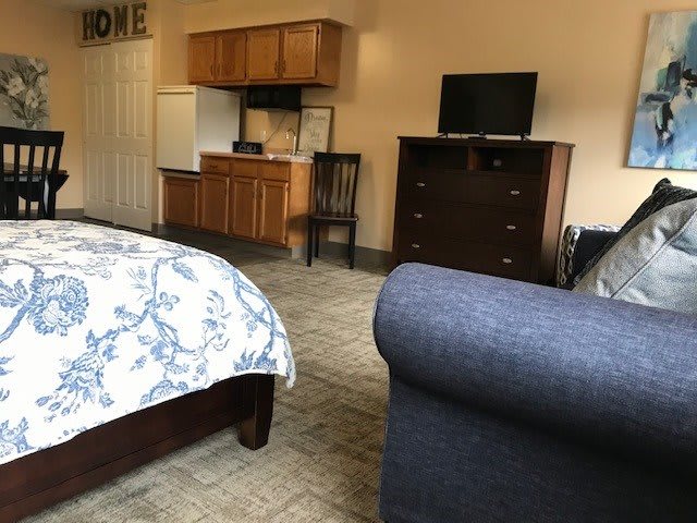 A cozy hotel room featuring a bed, small kitchenette, and a television.