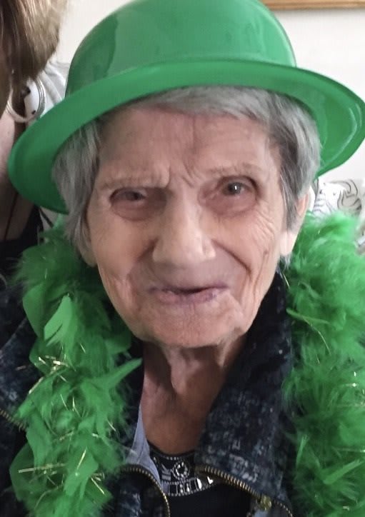 An elderly woman wearing a green hat and feather boa, celebrating with a festive spirit.