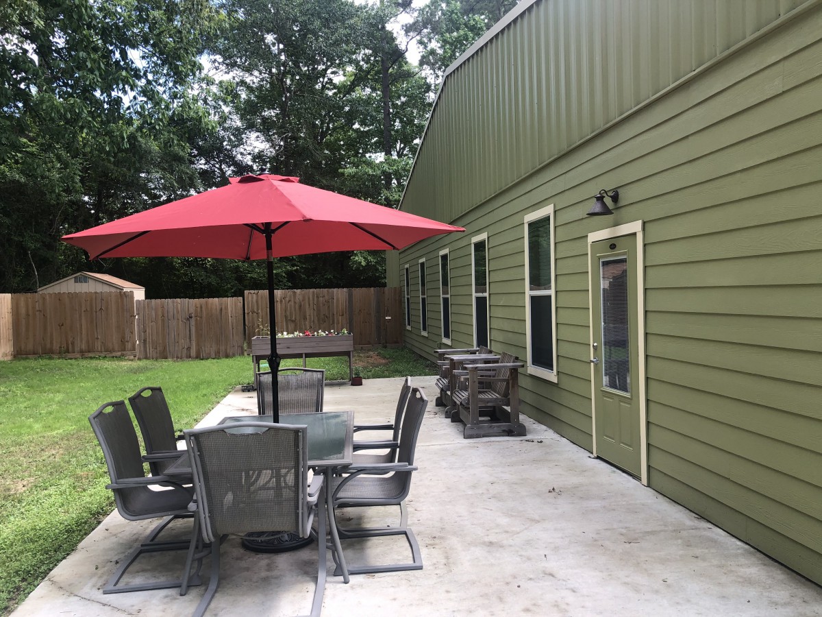 A backyard patio with a table, chairs, and a red umbrella next to a green building.