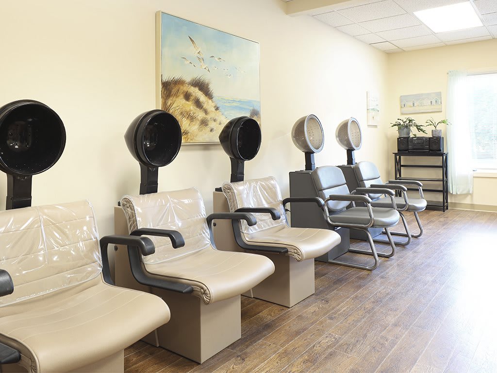 An empty hair salon with a row of chairs and hair dryers along the wall.