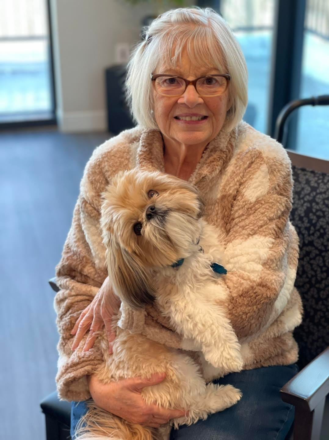 A smiling woman holding a fluffy dog indoors.
