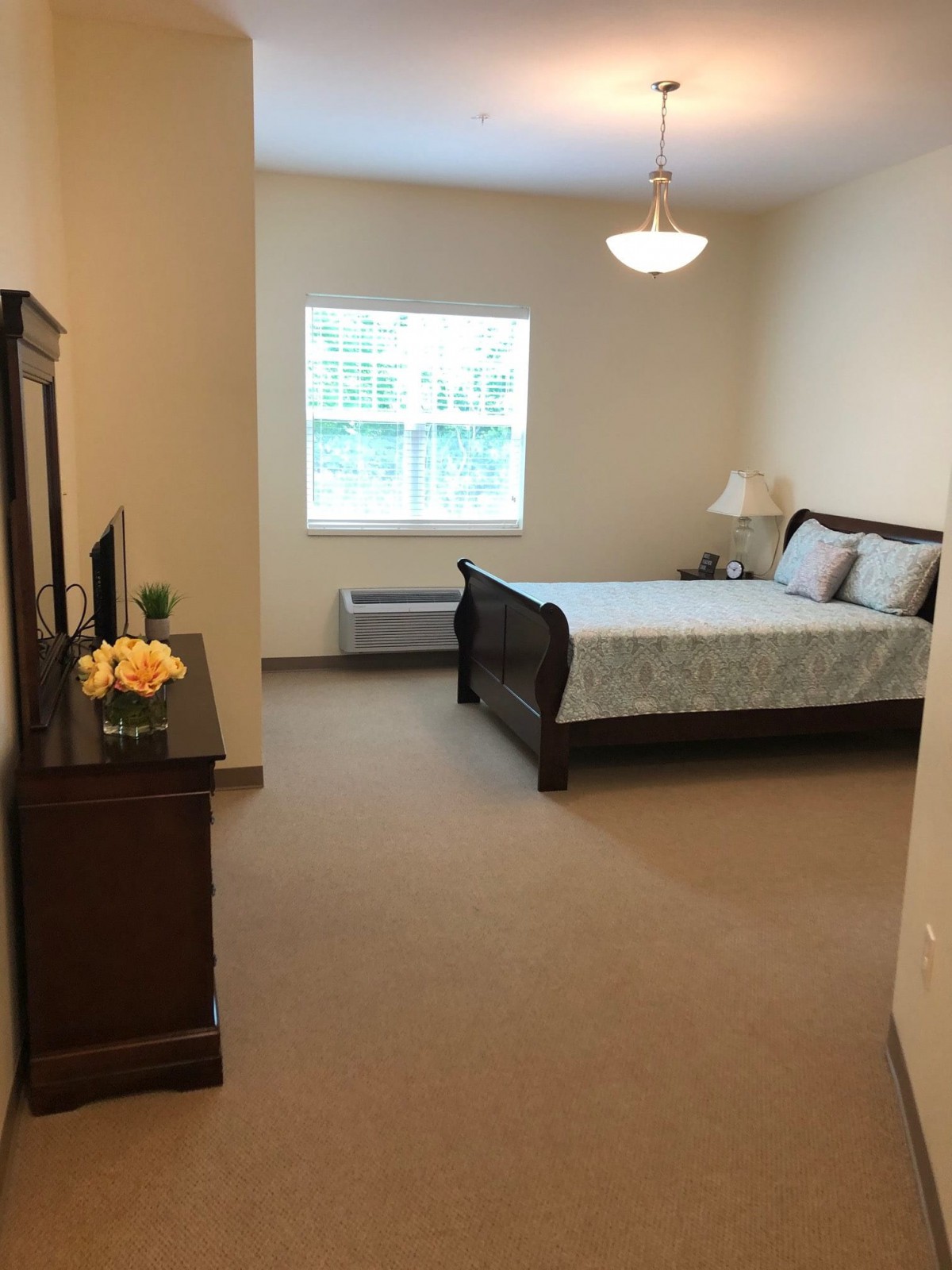 A cozy bedroom with a bed, dresser, and window allowing natural light.