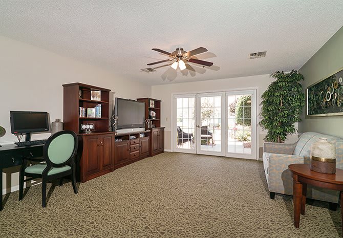 A cozy living room featuring a carpeted floor, ceiling fan, and French doors leading outside.