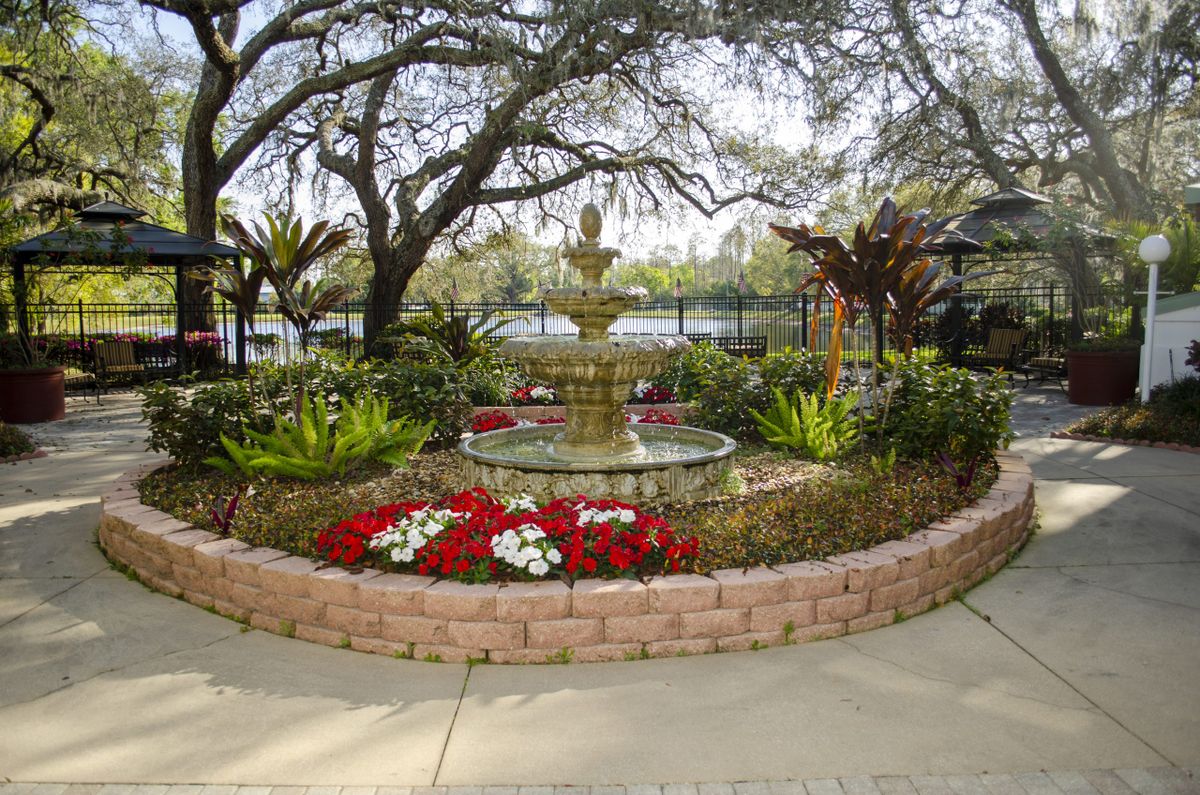 A scenic garden with a central fountain surrounded by flowers and greenery.