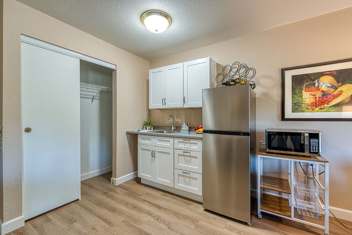 A compact kitchenette featuring a stainless steel fridge, white cabinets, and a microwave in a modern interior setting.