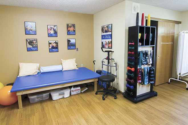 A well-equipped physical therapy room featuring a treatment table, exercise equipment, and motivational posters on the wall.
