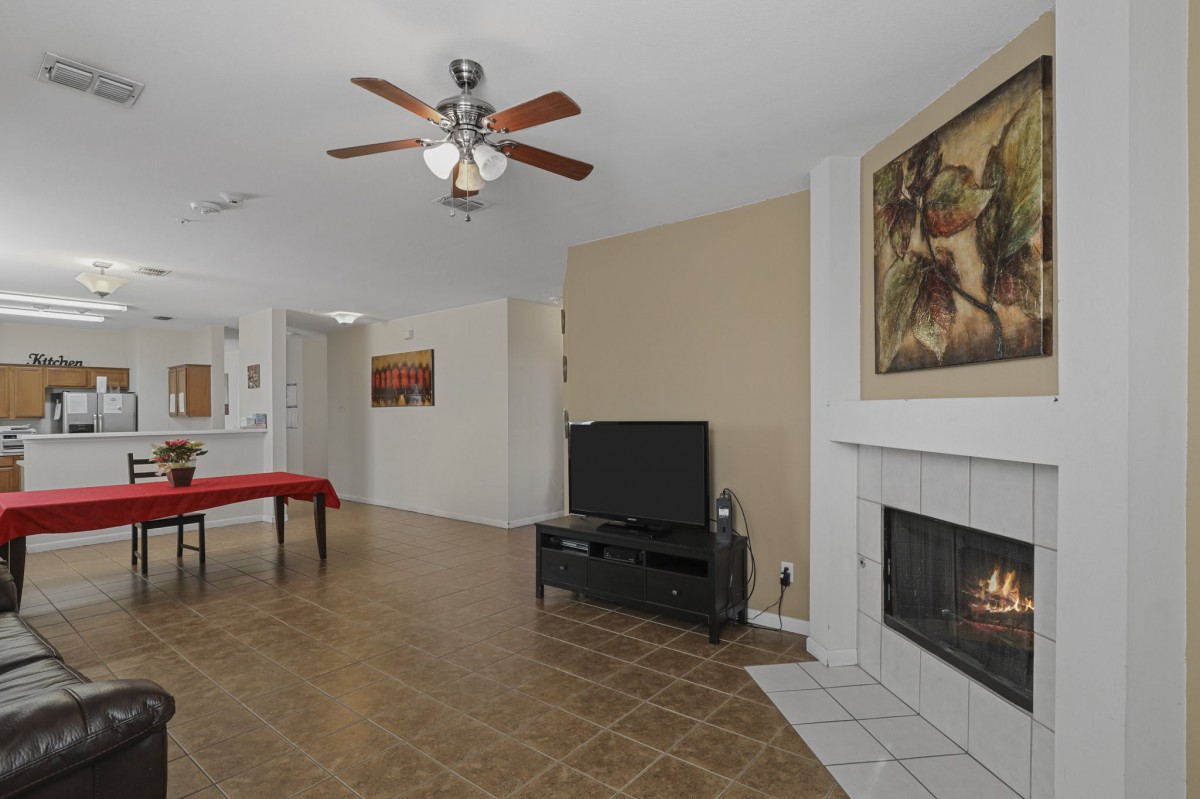 A cozy living room featuring a television, fireplace, and ceiling fan with artwork on the walls.