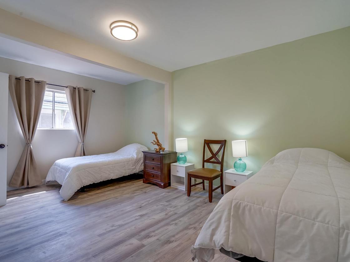 A cozy bedroom featuring two single beds, a nightstand with lamps, and natural light from the window.
