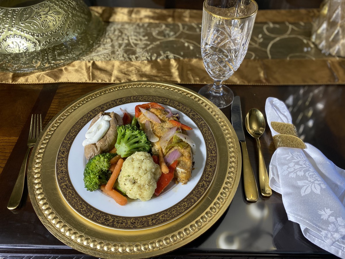 An elegant dining setup featuring a plated meal with vegetables and meat, accompanied by gold cutlery and glassware.