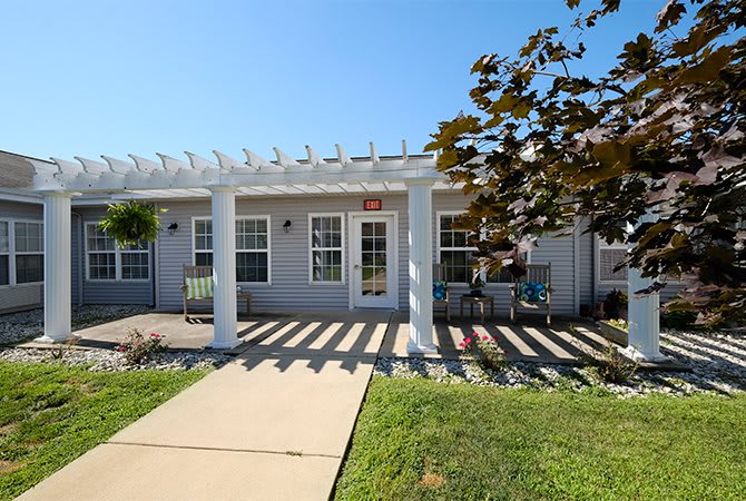 A cozy house with a pergola-covered porch and a pathway leading through the front yard on a sunny day.