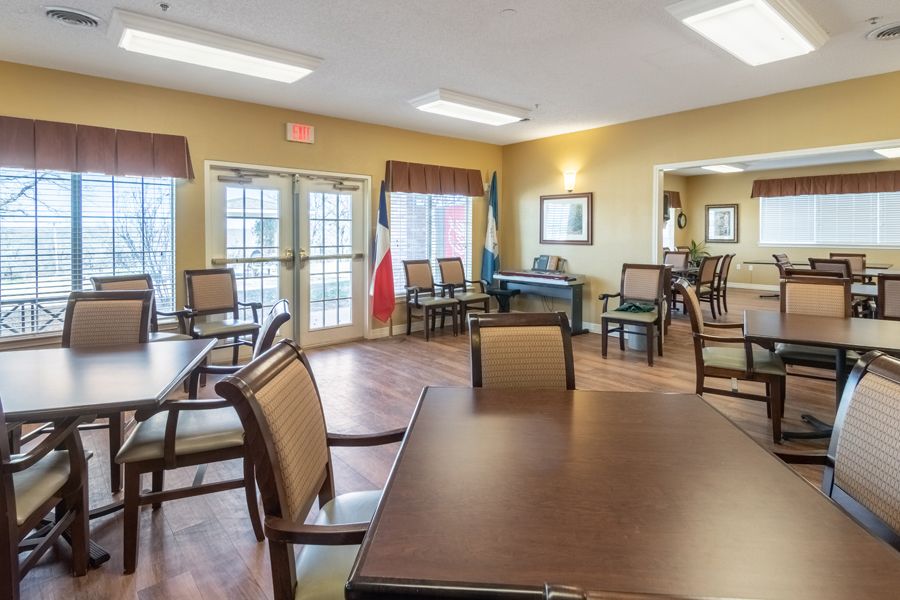 A well-lit dining area with tables and chairs arranged on a wood floor.
