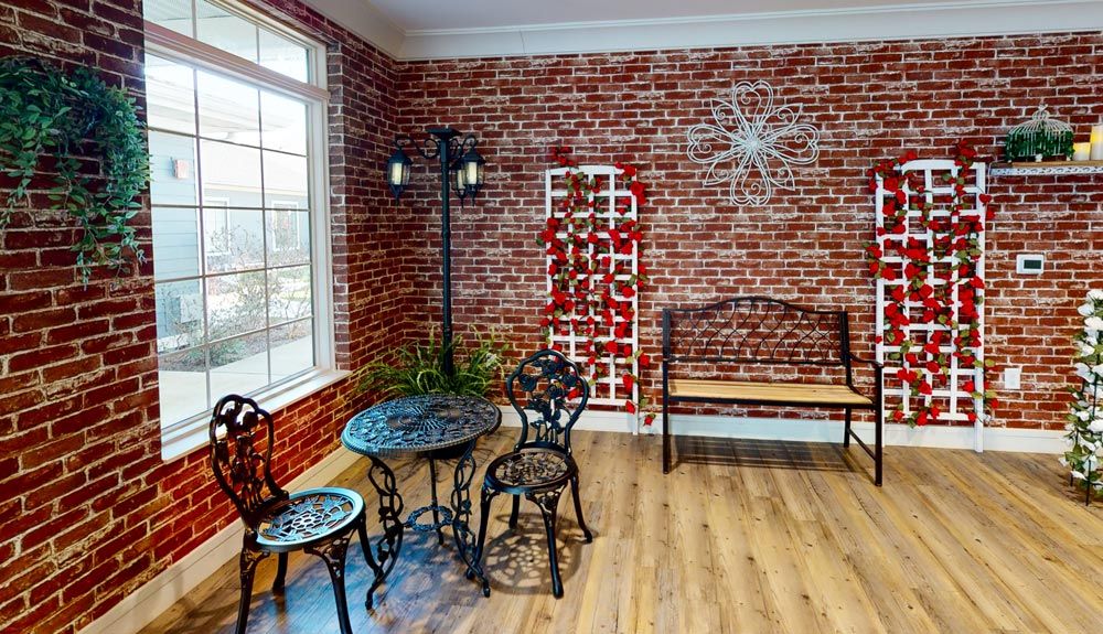 A cozy indoor space with a brick wall, featuring a metal table and chairs, a wooden bench, and decorative elements.