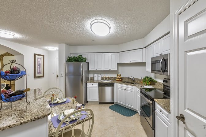 A modern kitchen with white cabinets and stainless steel appliances, complete with a small dining area.