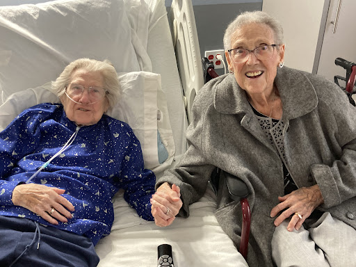 Two elderly women share a heartfelt moment in a hospital, showcasing the beauty of friendship and care.
