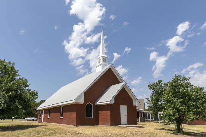 A traditional brick church with a prominent steeple stands under a partly cloudy blue sky.