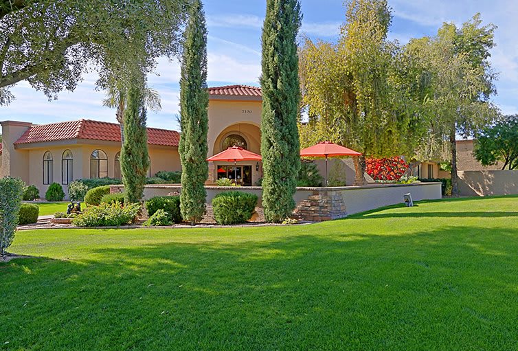 A scenic view of a building with red-tiled roof surrounded by lush green lawn and tall trees.