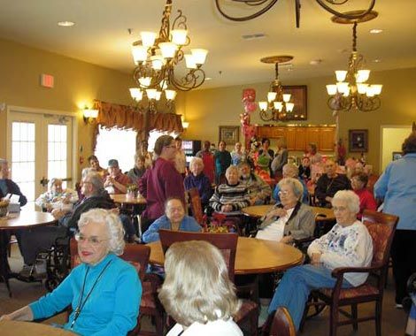 A lively gathering of seniors in a community room with chandeliers overhead.