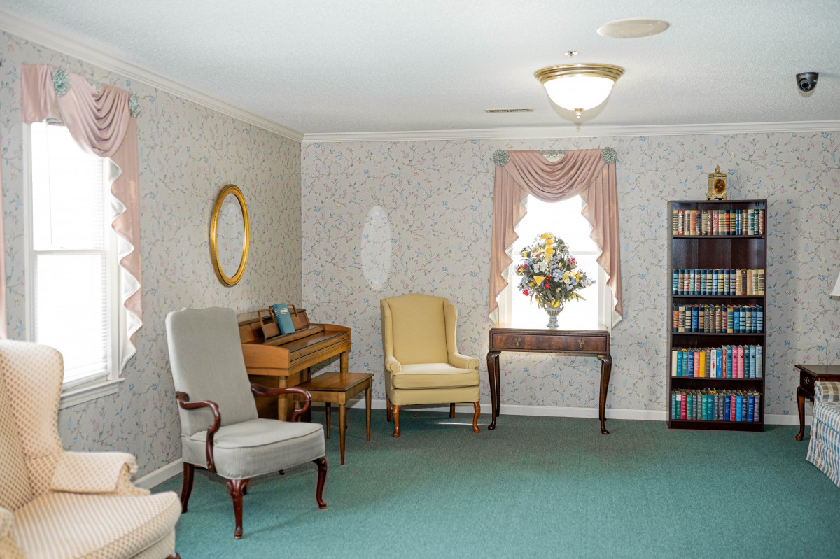 A cozy living room with vintage decor featuring armchairs, a bookshelf, and a floral arrangement by the window.